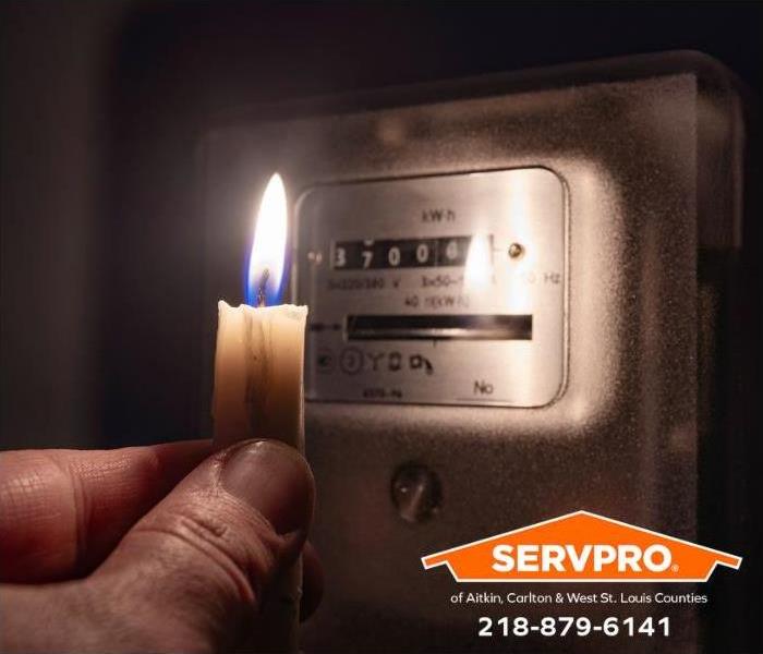 A person holds a candle up to an electrical power box during a power outage.